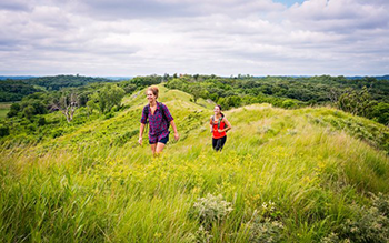 Two hikers ascend to the top of the Loess Hills in Western Iowa during a sunny summer day.