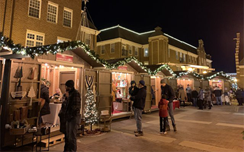 A small crowd wanders between vendor huts decorated in wreaths and holiday lights.