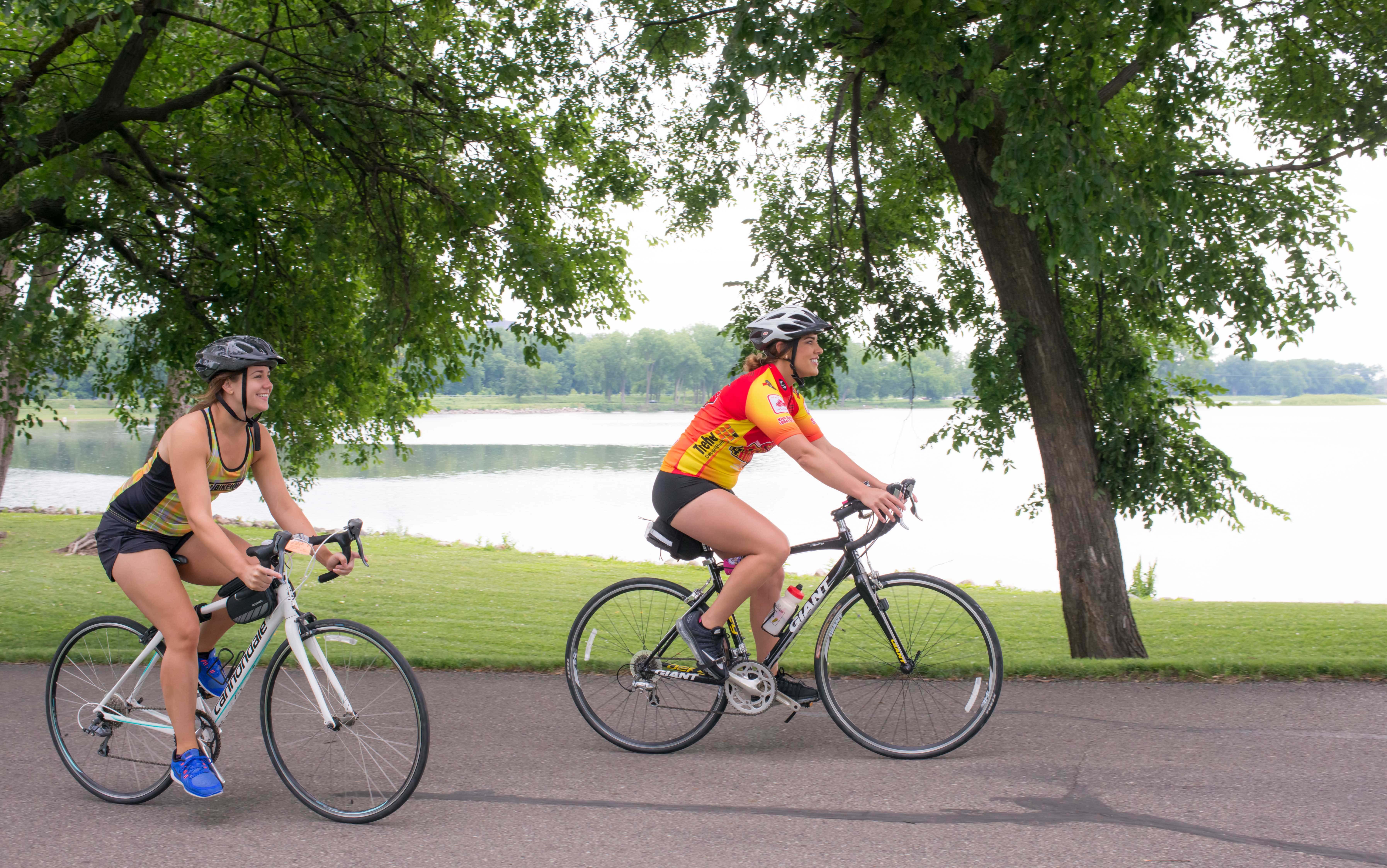 Two women ride bikes along a lakeside trail