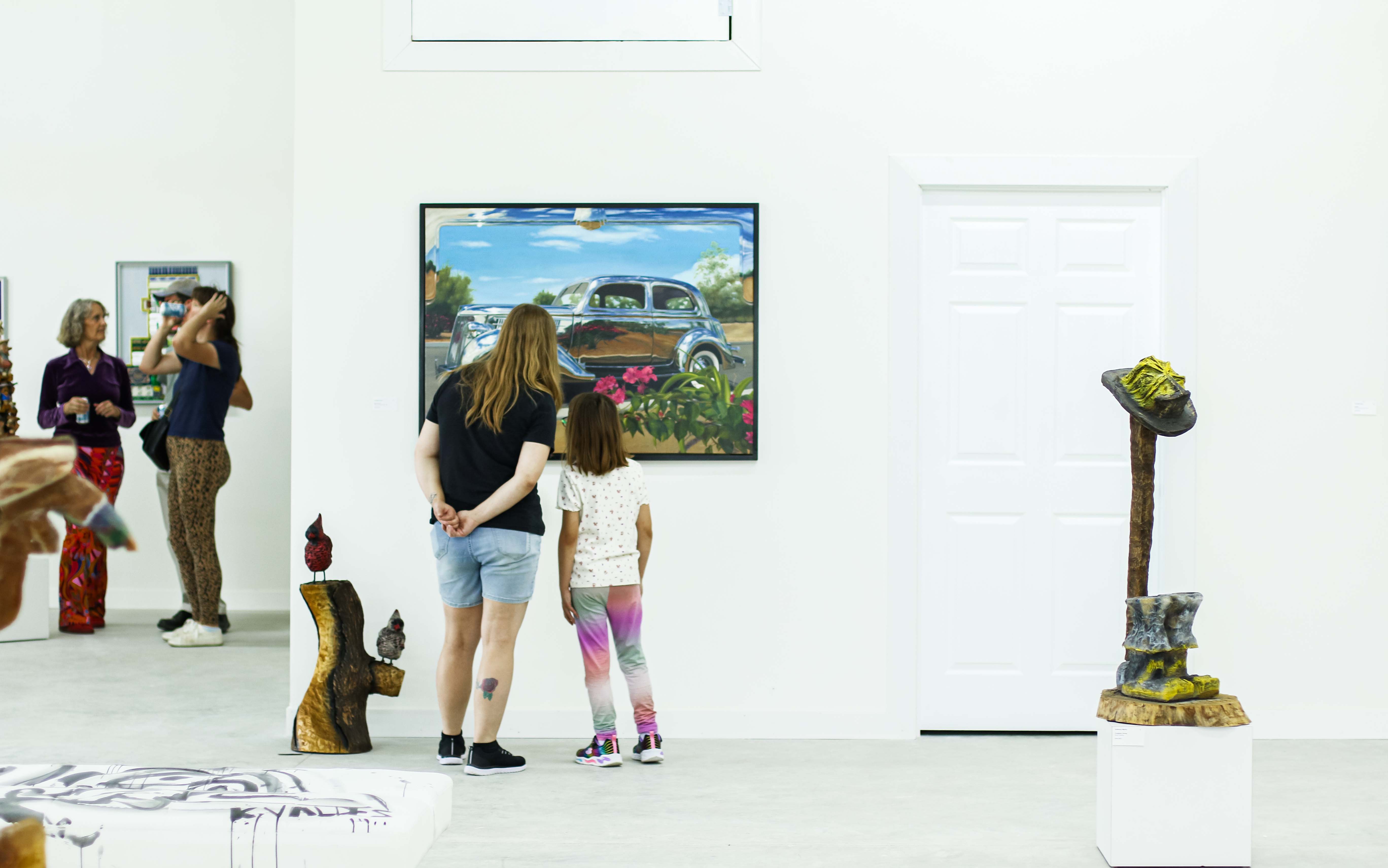 A mother and daughter admire a piece of hanging wall art in a gallery. 