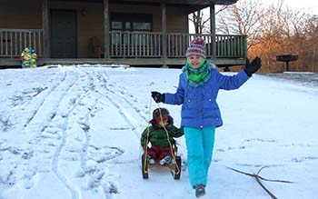 A girl in a purple winter coat pulls her younger brother on a sled through the snow.