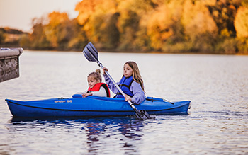 Two young girls paddle in a blue kayak.